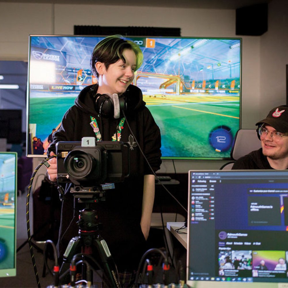 Esports students stood in front of digital screens with cameras